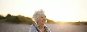 An older woman smiling on the beach.
